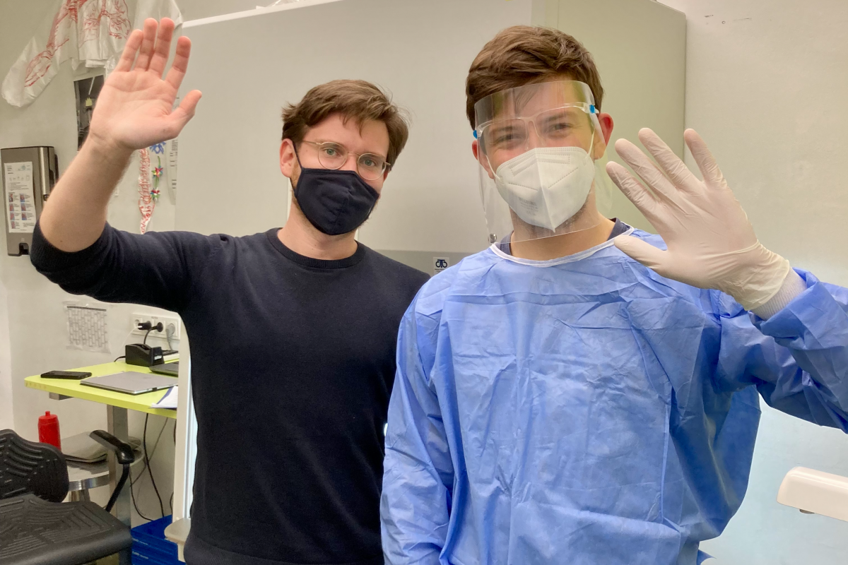 Sanitäter im Covid-Testraum der Marien Apotheke, die in die Kamera winken