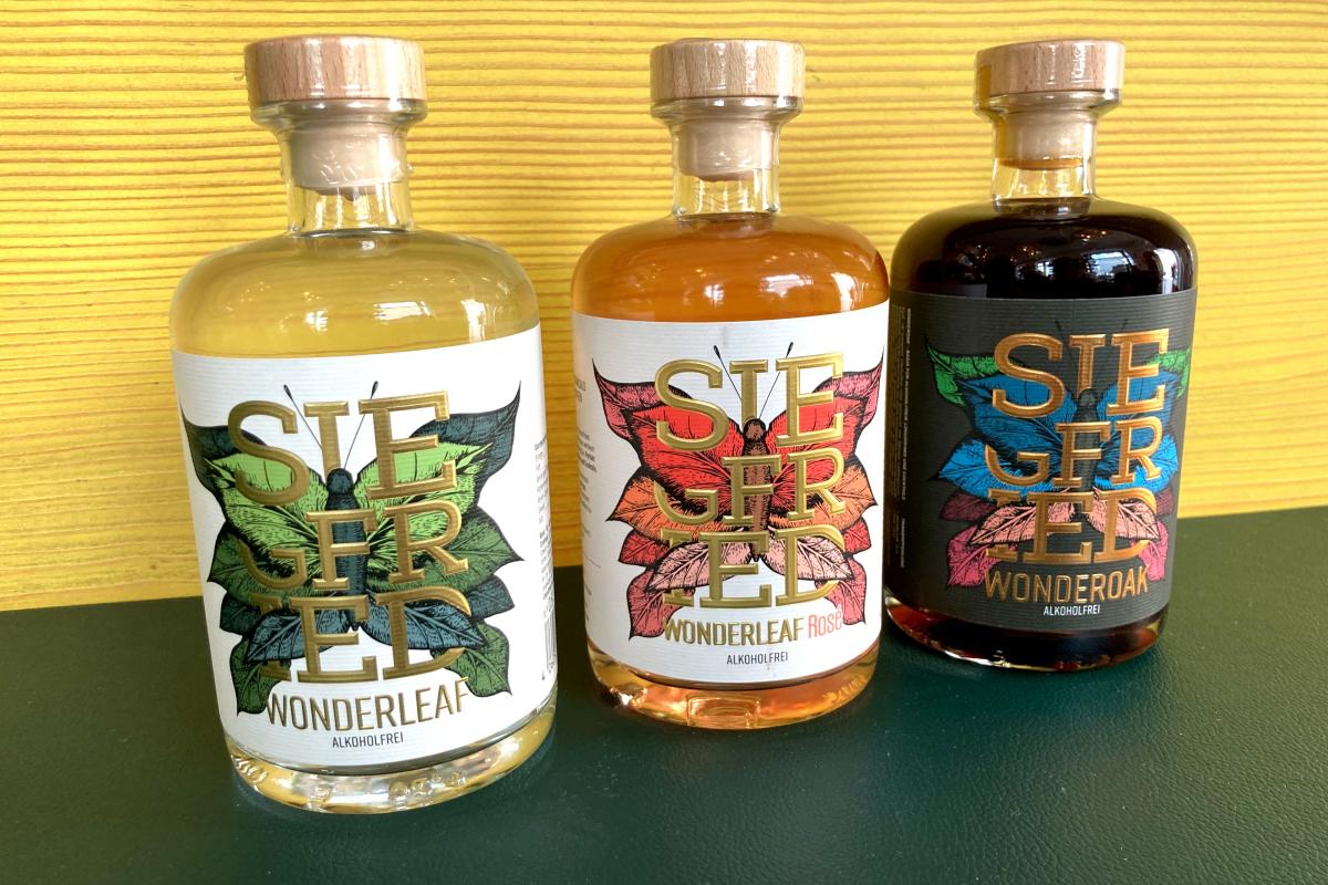 Drei verschiedene Sorten SIEGFRIED alkoholfreier Gin vor gelbem Hintergrund in der Marien Apotheke Wien