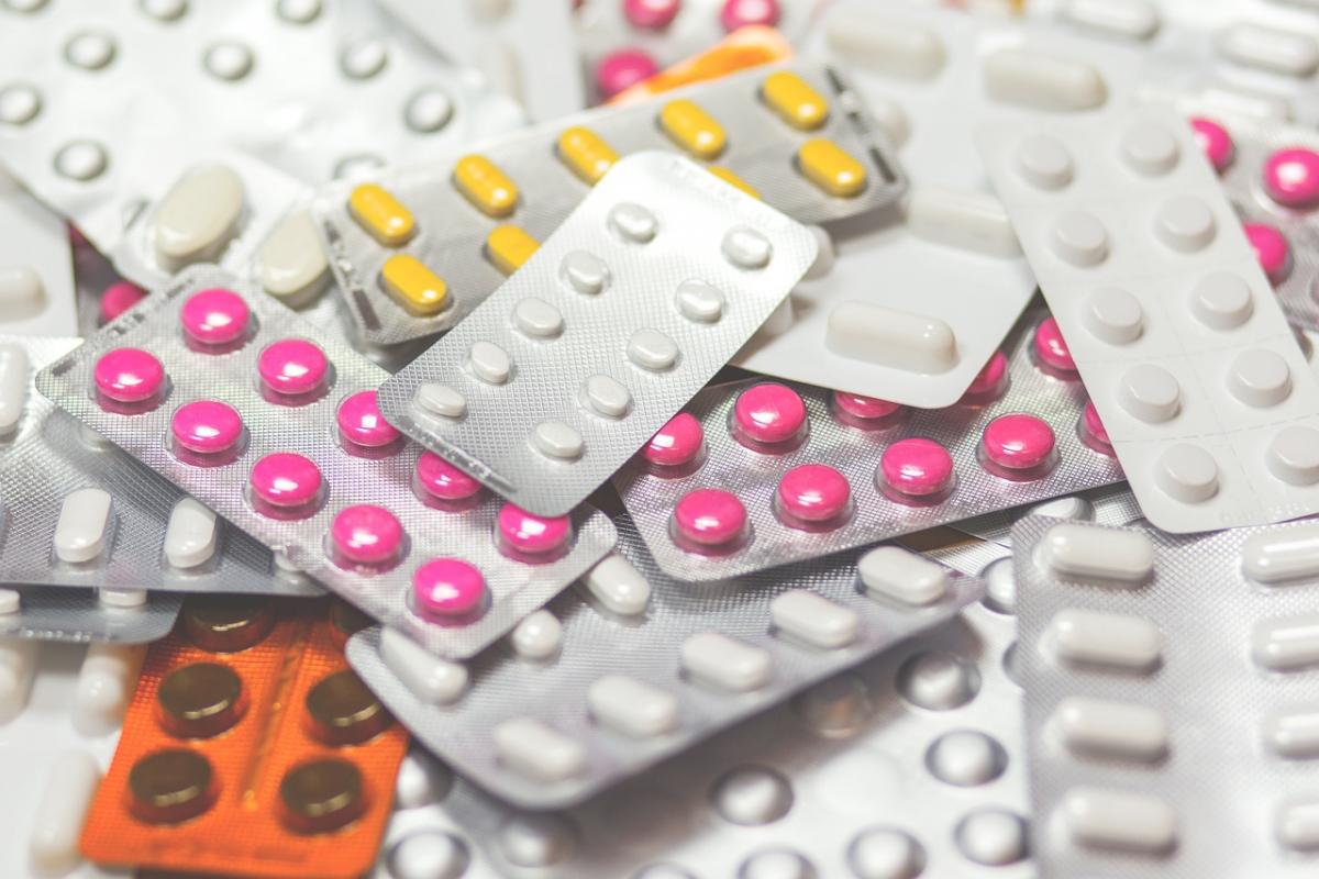 Verschiedene Medikamentenblister, die übereinander liegen und verschiedenfarbige Tabletten in pink, gelb und weiß enthalten