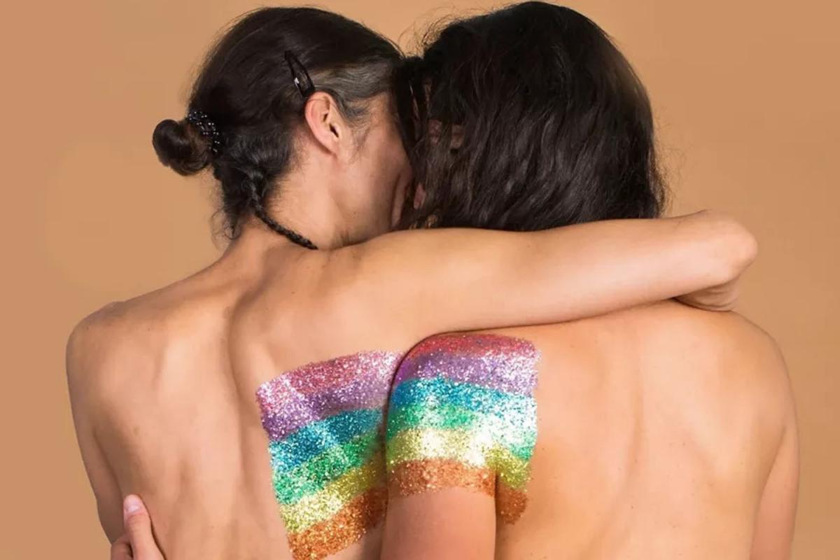 Eine nackte Frau und ein nackter Mann von hinten gesehen. Beide haben Regenbogenfarbenen Glitzer am Rücken