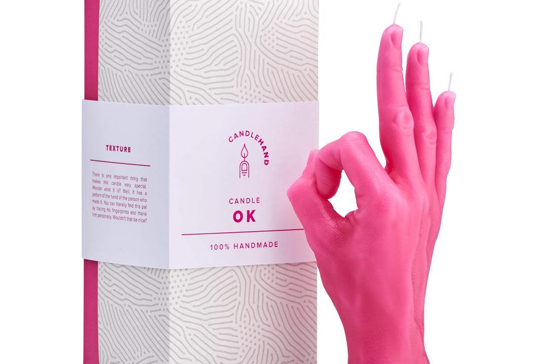 Candlehand Kerze in pink neben der Verpackung. Die Kerze in Handform zeigt die Geste OK.