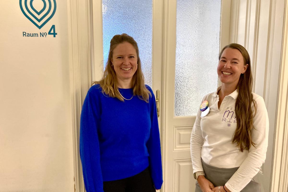 Bild von Miriam Alvarado von der an.doc.stelle und Ines Werzinger von der Marien Apotheke, die vor einem Raum mit Glastür stehen. An der Wand steht links daneben