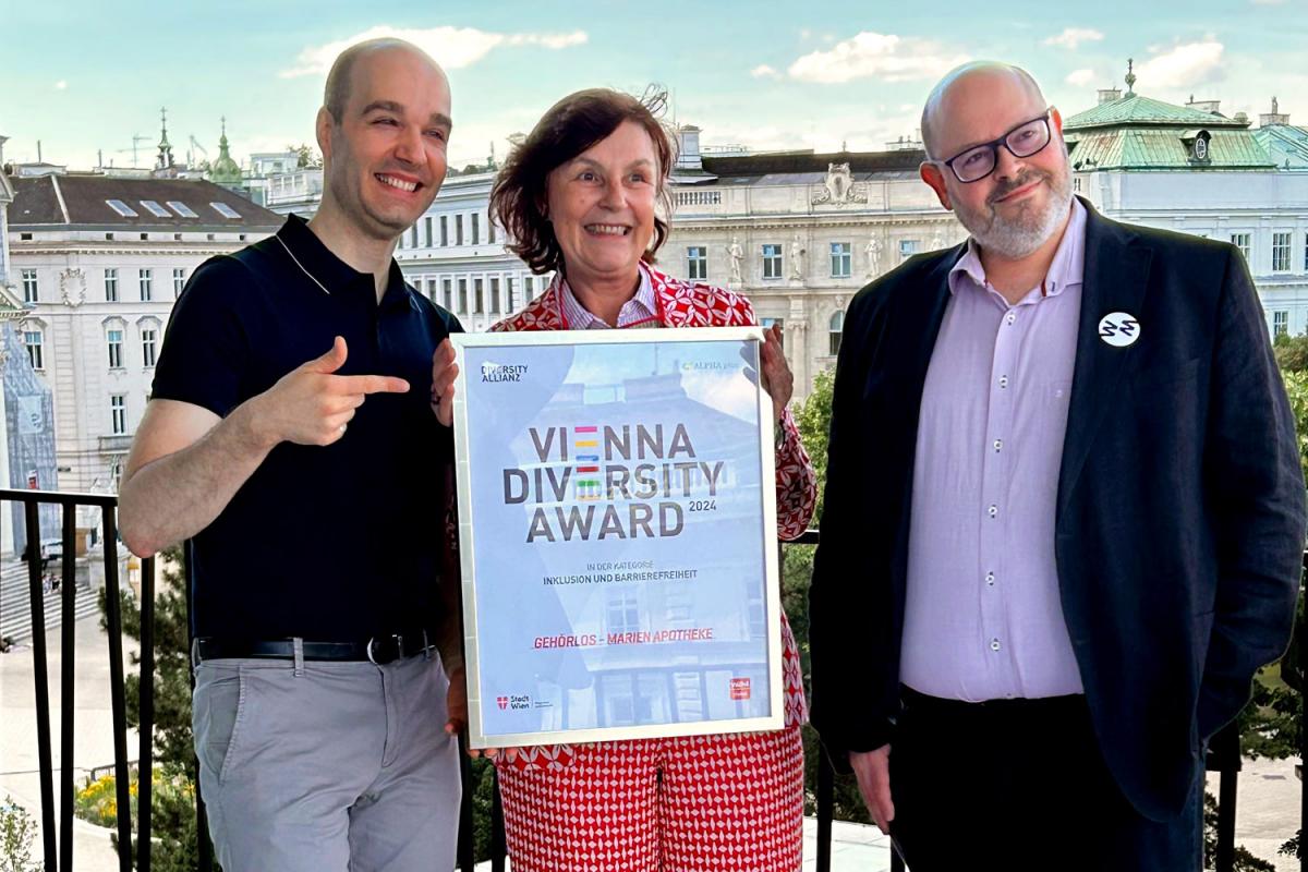 Sreco Dolanc, Karin Simonitsch und Wien Museums-Direktr Matti Bunzl stehen auf der Terrasse des Wien Museums. Karin Simonitsch hält die Auszeichnung